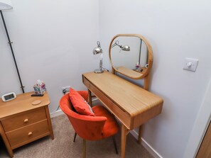 A small, tidy room with a wooden desk, a chair, a mirror, a lamp, and a bedside table with a clock and a tissue box. - Amber Rose (Berwick-upon-Tweed)