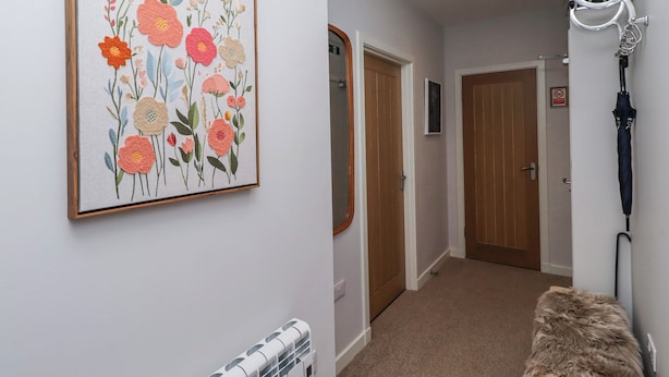 A hallway with a framed floral artwork, a radiator, a fur-covered bench, and a door with a no-smoking sign. - Amber Rose (Berwick-upon-Tweed)