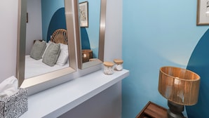 A bedroom with a bed, a bedside table, a mirror, a wicker lamp, and a framed picture on the wall. - Amber Rose (Berwick-upon-Tweed)