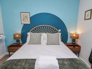 A bed with a rattan headboard, two bedside lamps, and a framed picture on the wall. - Amber Rose (Berwick-upon-Tweed)