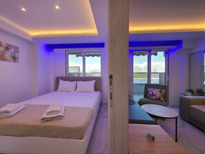 A modern hotel room with a large bed, a small seating area, and a balcony with a view.