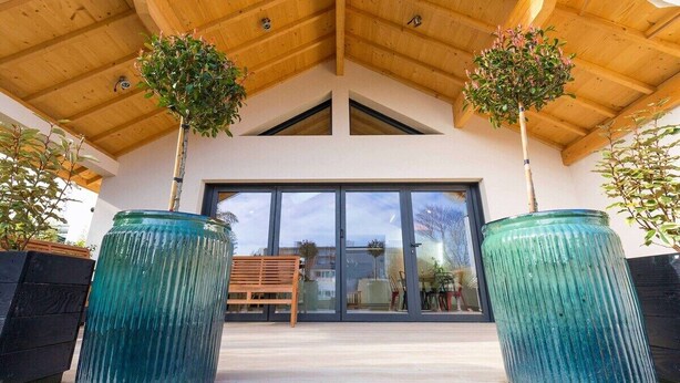A modern building with a wooden ceiling, large glass doors, and two potted plants. - Le Balzac – Architect-designed home 132m² (Dijon)
