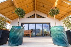 Un edificio moderno con techo de madera, puertas de cristal grandes y dos plantas en macetas.