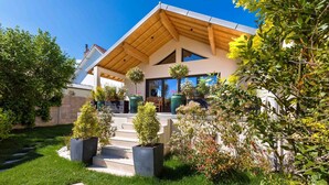 A modern house with a sloped roof, a front porch with steps, and a garden with various plants and shrubs. - Le Balzac – Architect-designed home 132m² (Dijon)