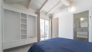 Un dormitorio con una cama grande, un armario, un baño con espejo y una puerta corrediza de cristal a un balcón.