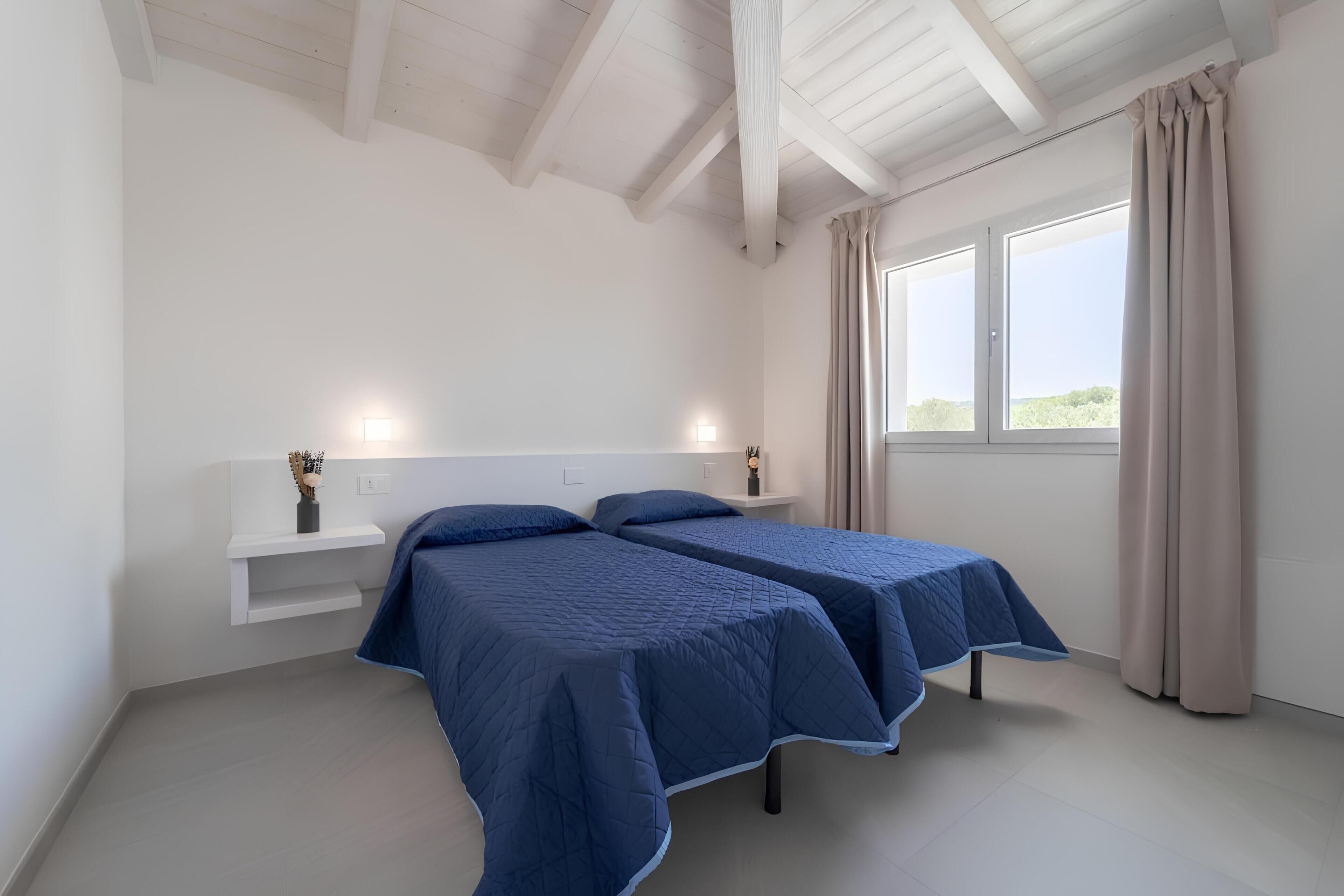 Une chambre avec deux lits, une fenêtre avec des rideaux, un mur blanc et un plafond avec des poutres en bois.