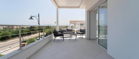 A balcony with a sofa, chairs, and a table, overlooking a road and distant buildings.