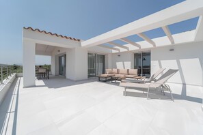 En moderne tagterrasse med fliset gulv, et beige loungesæt og en solstol.
