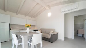 Una cocina moderna con armarios blancos, una mesa de comedor con sillas, un sofá y un equipo de aire acondicionado.