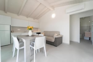 Una cocina moderna con armarios blancos, una mesa de comedor con sillas, un sofá y un equipo de aire acondicionado.
