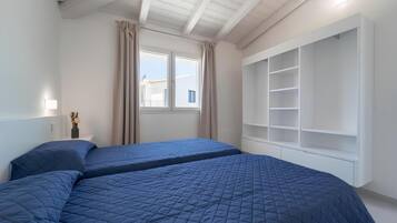 Une chambre avec deux lits, une fenêtre avec des rideaux, une table de chevet avec une lampe et une armoire intégrée.