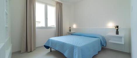 A bedroom with a bed, a window, a bedside table, and a nightstand.