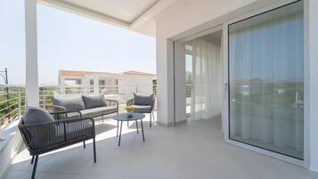 A balcony with a sofa, chairs, and a small table, with a view of buildings in the background.