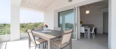 A modern outdoor dining area with a table and chairs, a glass door leading to an interior space, and a view of the landscape.