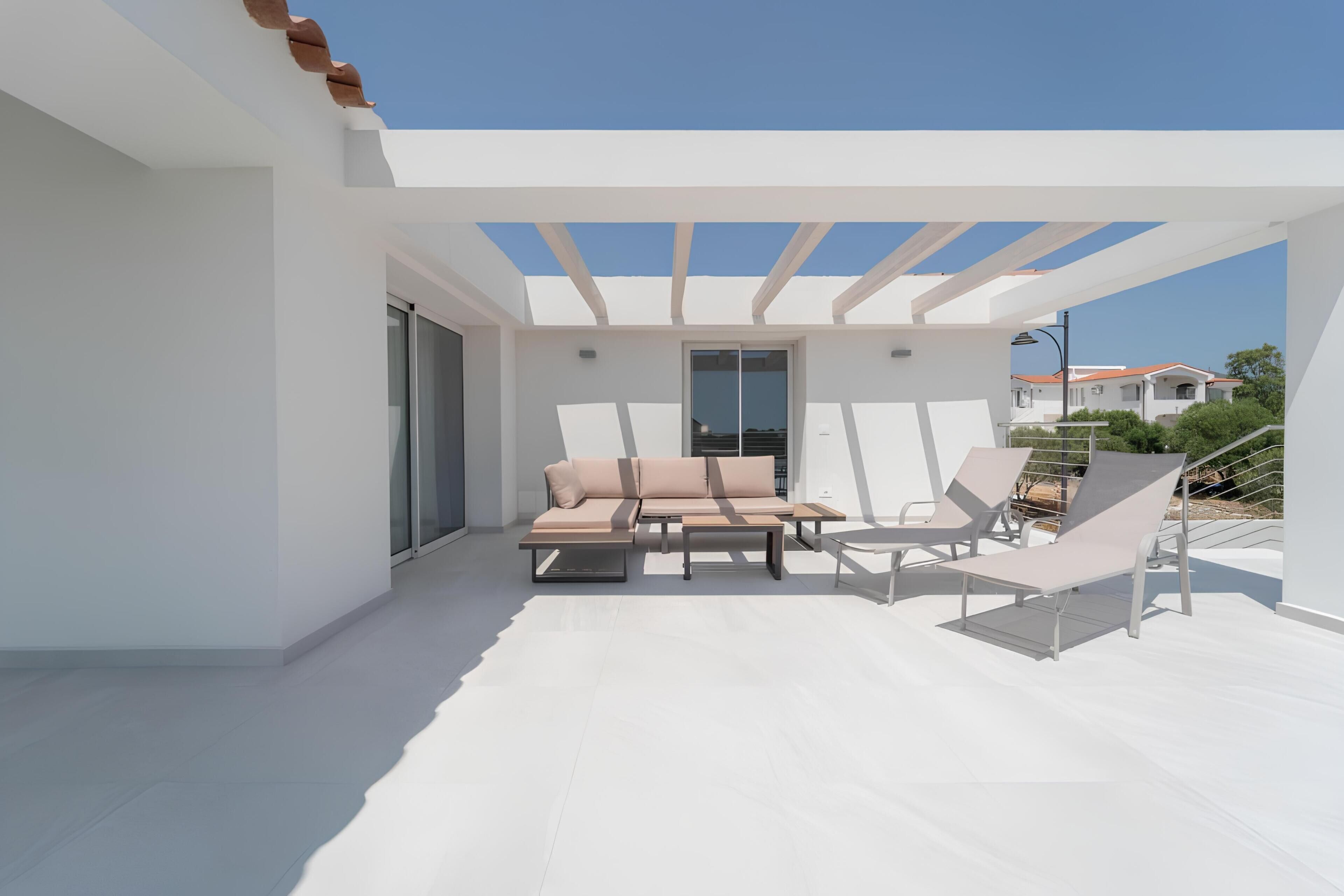A modern outdoor patio with a sofa, chairs, and a glass door leading to a balcony.