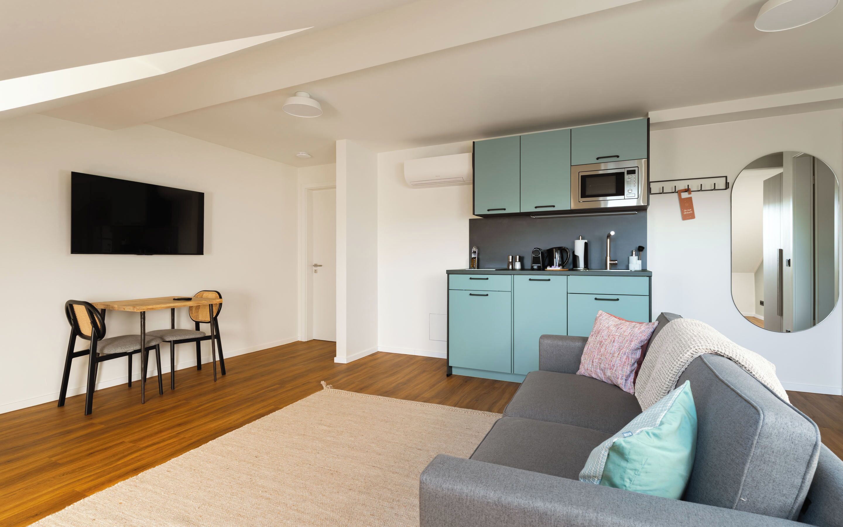 Een compacte leefruimte met een kitchenette, een eethoek en een zithoek met een bank en een televisie.