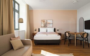 A hotel room with a bed, a sofa, a dining table with chairs, and artwork on the wall. - Limehome Gelsenkirchen Hochstr. (Gelsenkirchen)