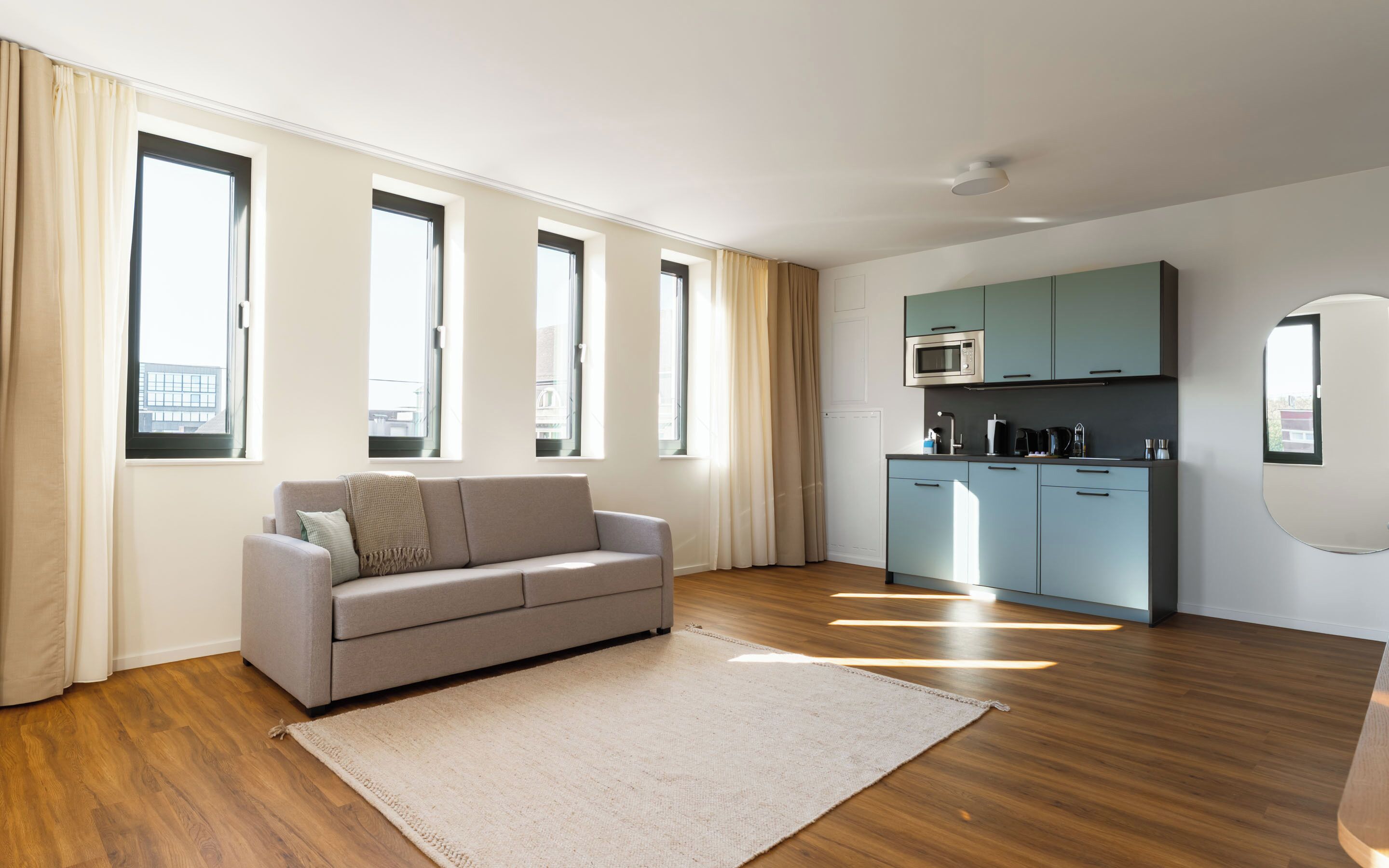 Una sala de estar moderna con un sofá, una cocina equipada y ventanas amplias.