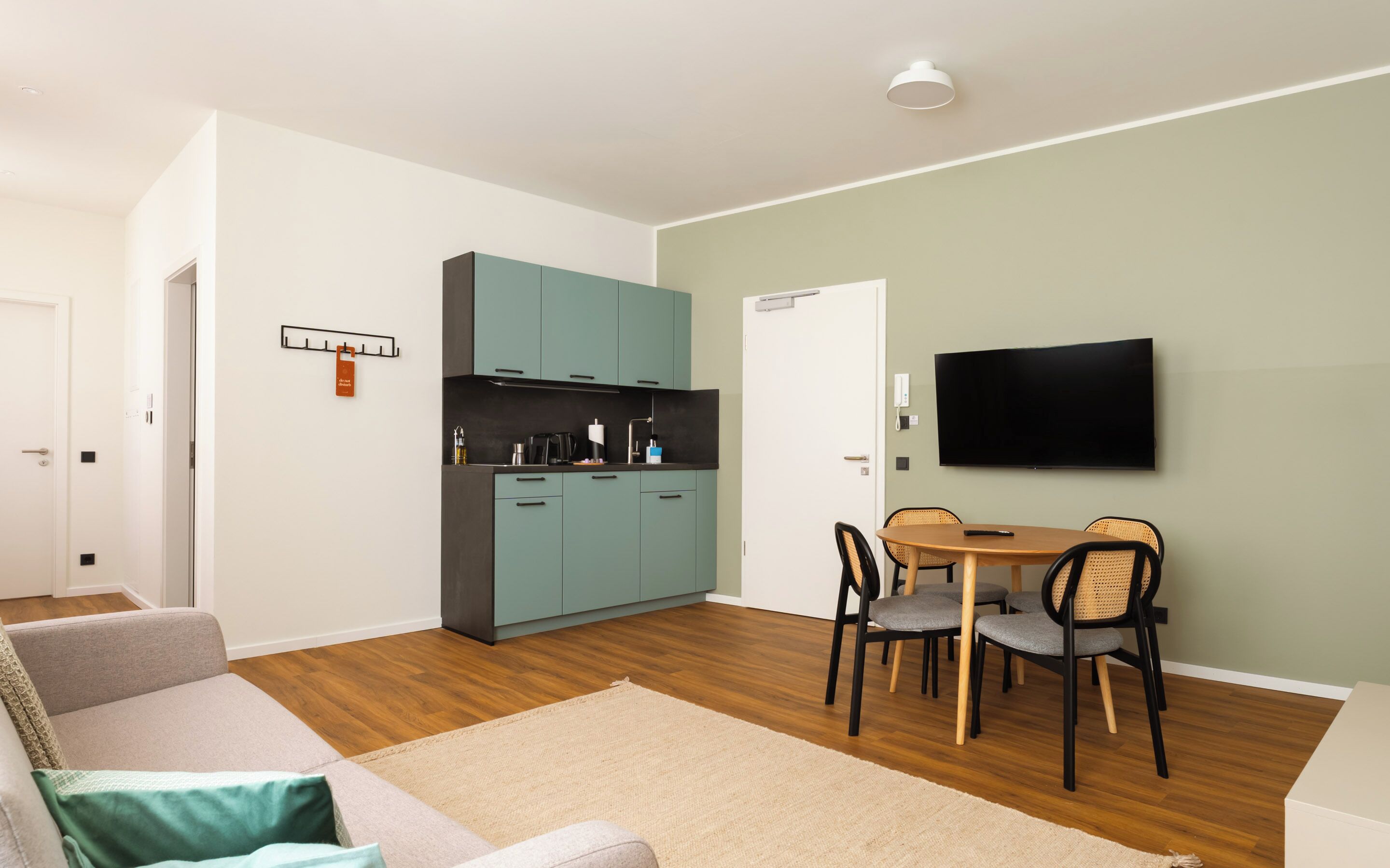 Un espace de vie compact comprenant un coin cuisine, un coin repas, un canapé et un téléviseur fixé au mur.