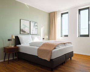 A bedroom with a bed, two bedside tables, a window, and artwork on the wall. - Limehome Gelsenkirchen Hochstr. (Gelsenkirchen)