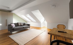 A modern loft with a sloped ceiling, a sofa, a dining table, and a chair. - Limehome Gelsenkirchen Hochstr. (Gelsenkirchen)