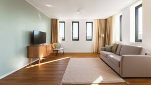 Una sala de estar moderna con un televisor de pantalla plana, un sofá, un sillón y un ventanal grande.