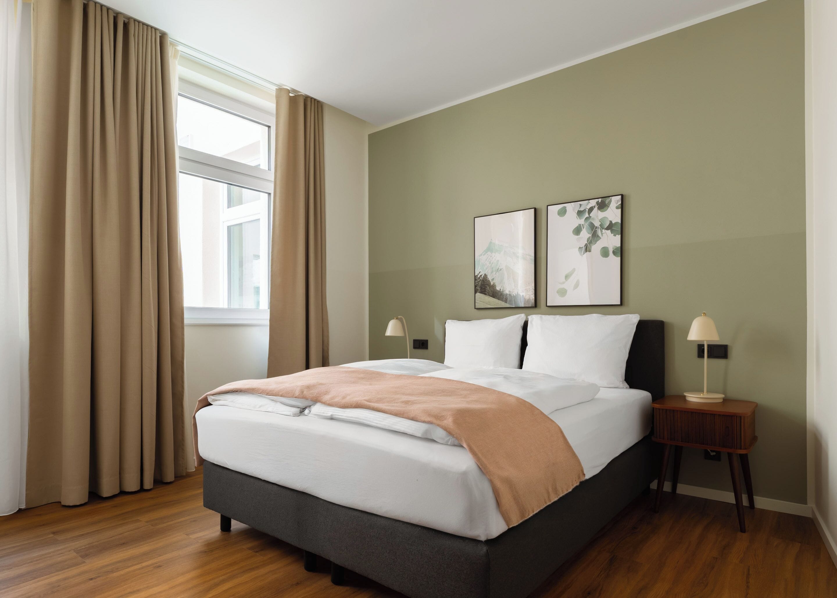 Un lit bien fait, recouvert d’une couvre-lit blanche et beige, avec une tête de lit foncée et deux lampes de chevet.
