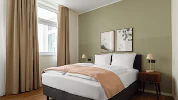 Una cama bien hecha con una colcha blanca y beige, un cabecero oscuro y dos lámparas de noche.