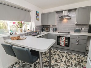 Eine moderne Küche mit grauen Schränken, einer weißen Arbeitsplatte, einem eingebauten Backofen und einem strukturierten Boden.