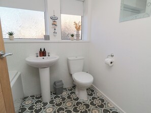 A bathroom with a white sink, toilet, patterned floor tiles, a small trash bin, and a window with a beach-themed decoration. - Coastal Retreat (Scarborough)
