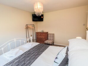 Ein Schlafzimmer mit Bett, Schminktisch, Stuhl, Kleiderständer und einem Fernseher an der Wand.