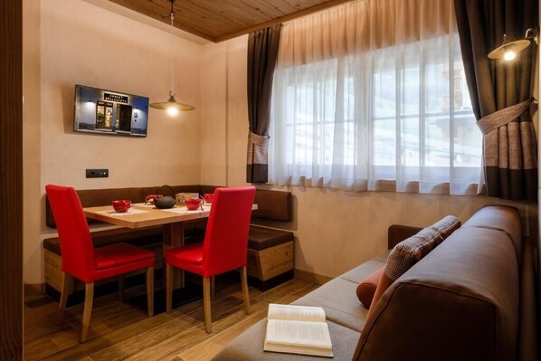 A cozy room with a dining table, red chairs, a sofa, and a window with curtains. - Chalet Bellavista (Livigno)