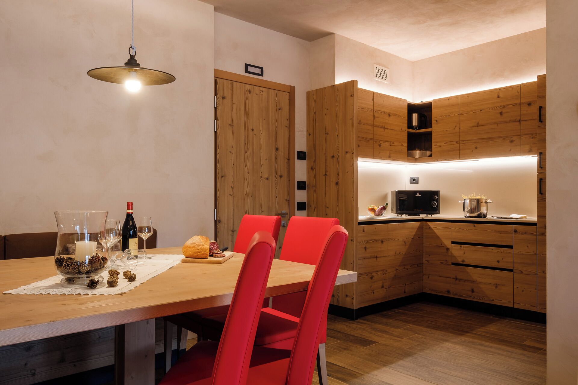 Eine moderne Küche mit Holzausstattung, einem Esstisch mit roten Stühlen und einer Mikrowelle.
