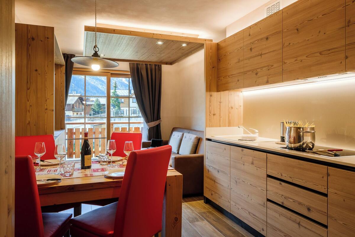 A dining area with a wooden table, red chairs, and a view of mountains through large windows.