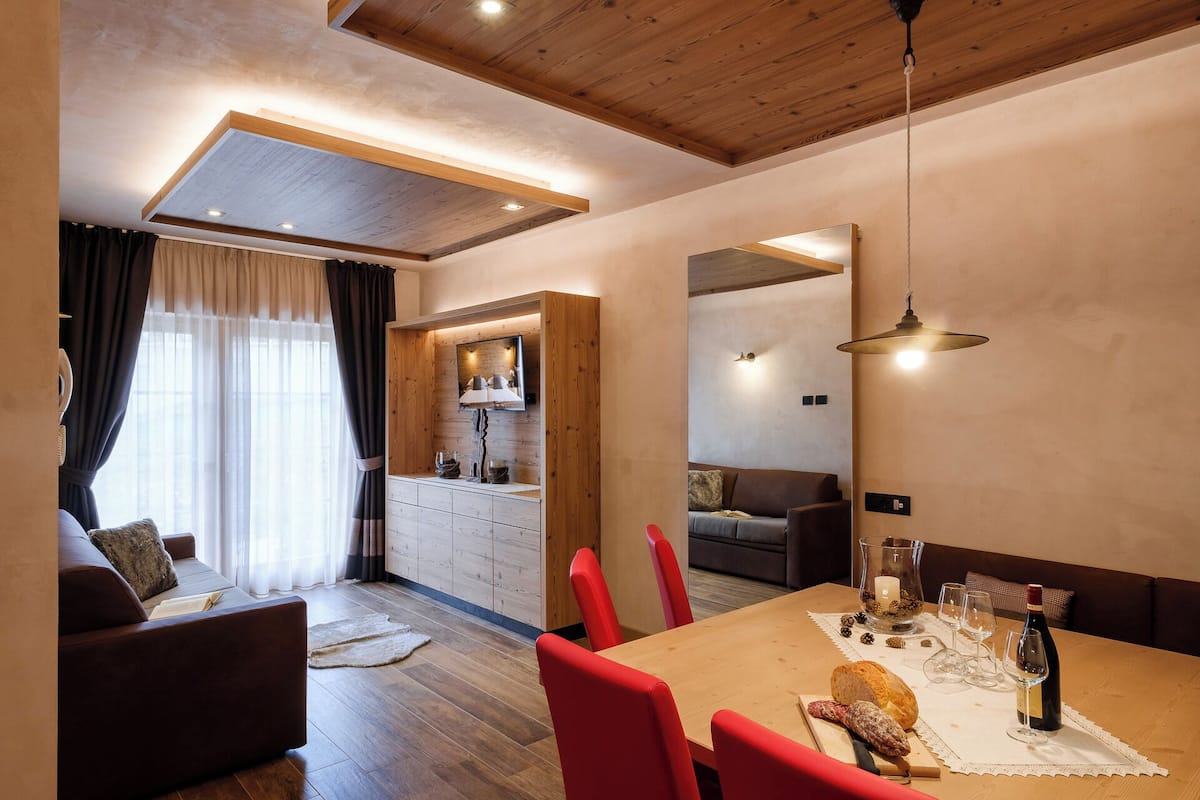 A dining area with a wooden table, red chairs, and a mirror above.