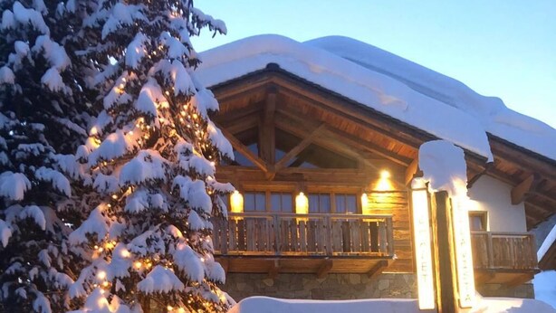 Un edificio cubierto de nieve con un balcón de madera y un árbol de Navidad iluminado.