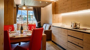 Un comedor con una mesa de madera, sillas rojas y vistas a montañas a través de una ventana.