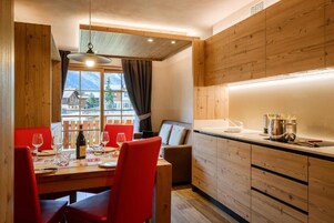 Un comedor con una mesa de madera, sillas rojas y vistas a montañas a través de una ventana.