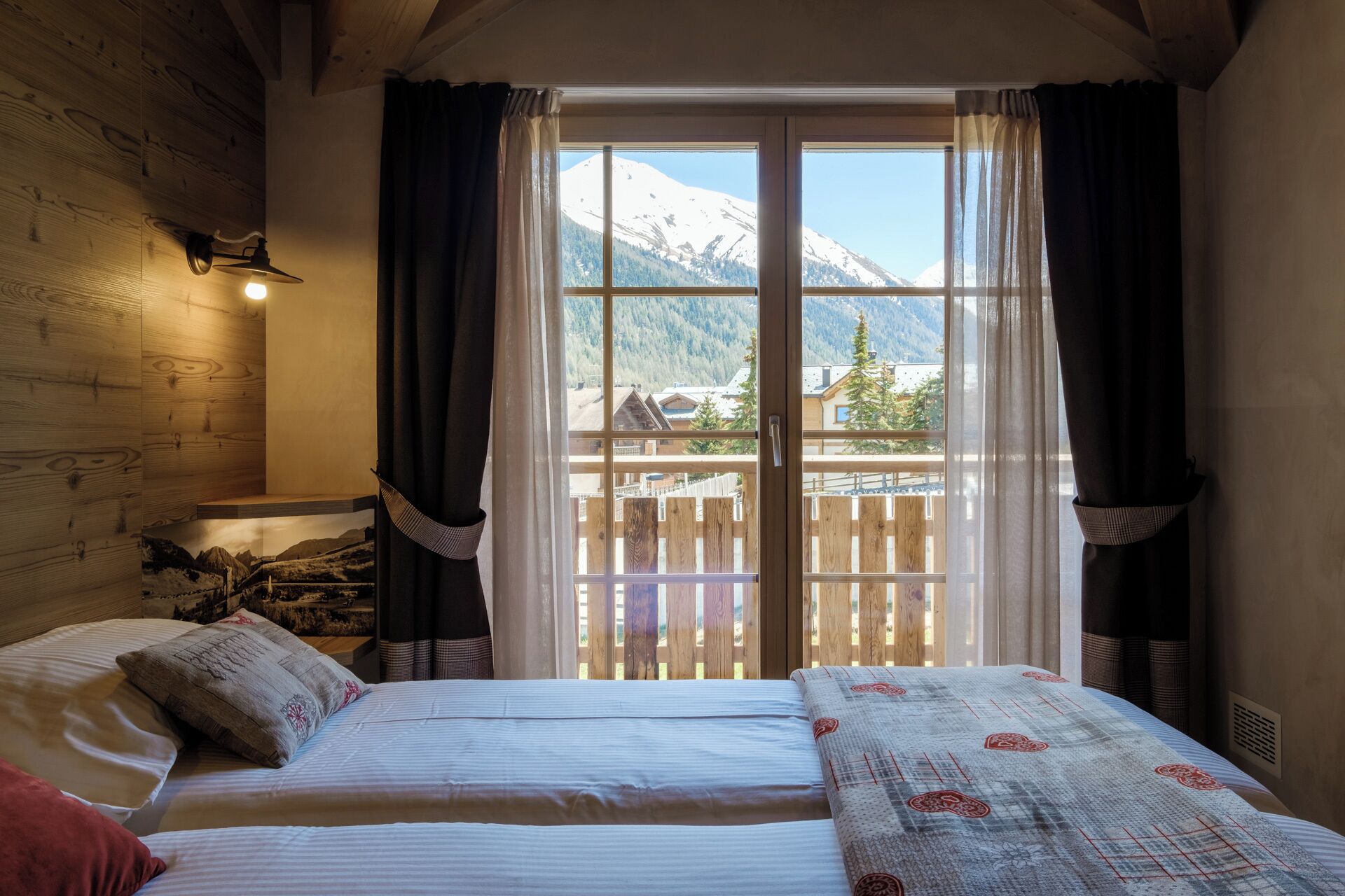 A room with two beds, a wooden headboard, a window with curtains, and a mountain view.