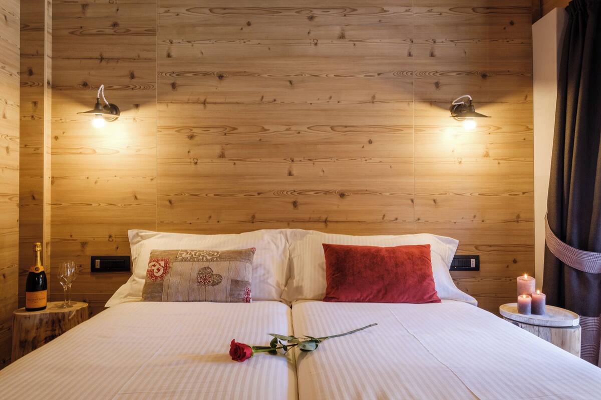 A wooden-paneled room with a bed, two bedside lamps, a small table with candles, and a bottle of champagne.