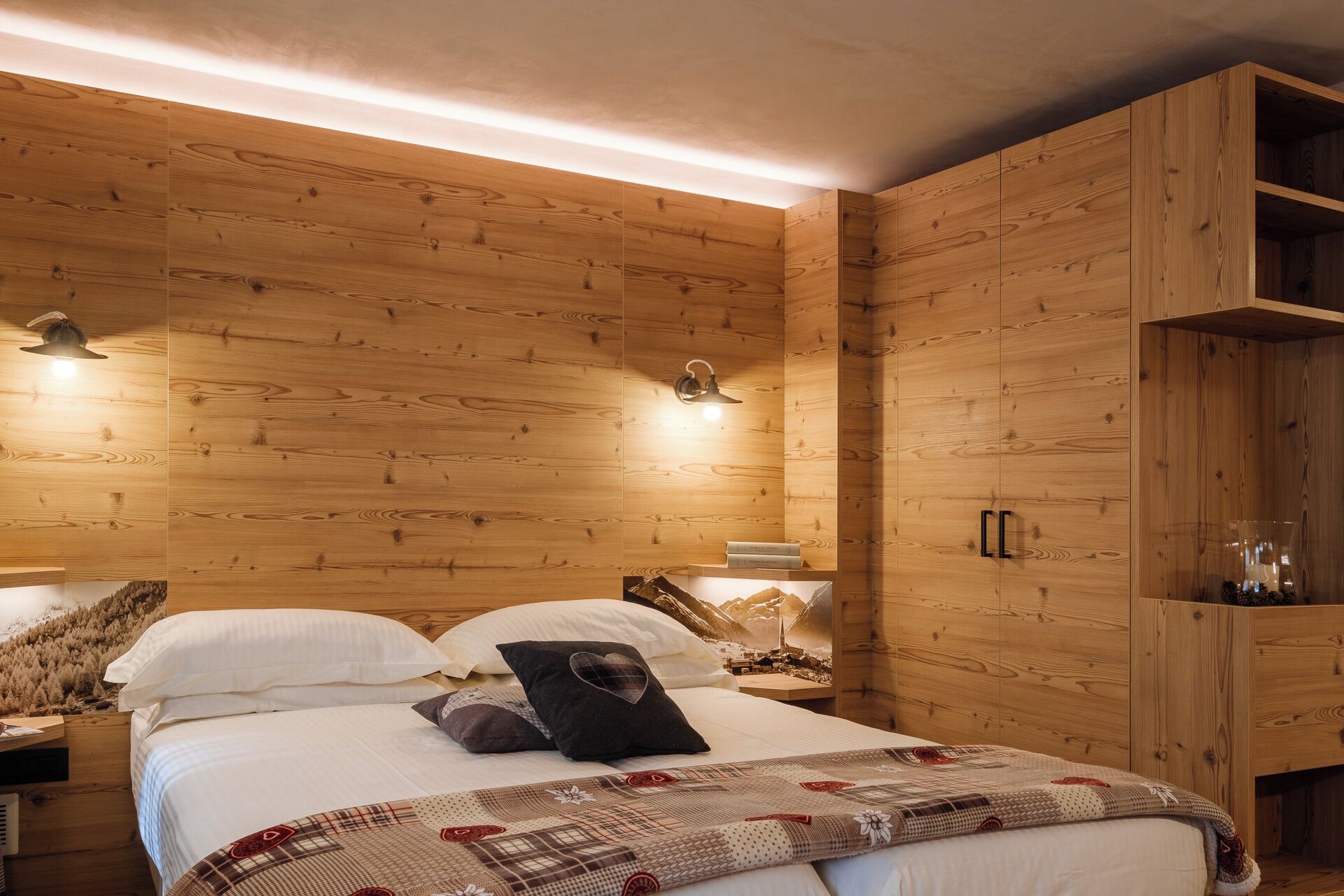 A wooden-paneled bedroom with a bed, pillows, a nightstand, and a wall-mounted lamp.