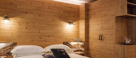 A wooden-paneled bedroom with a bed, pillows, a nightstand, and a wall-mounted lamp.