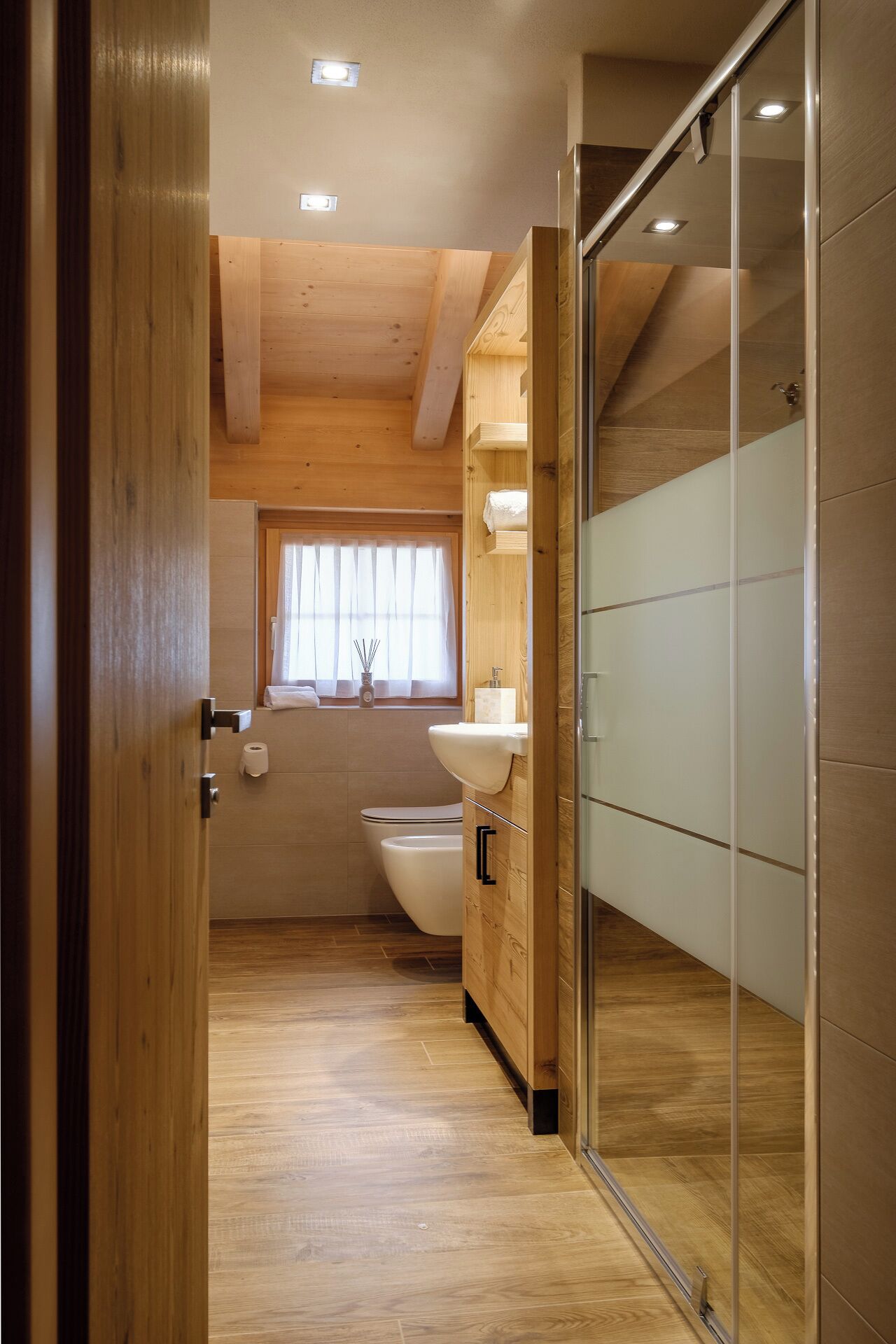 Een moderne badkamer met houten balken, een toilet, wastafel en een douchecabine van glas.