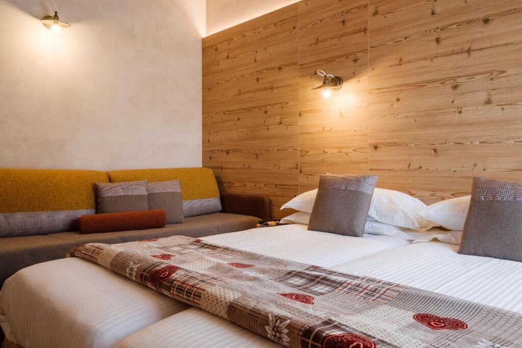 Un dormitorio con cabecera de madera, sofá cama y cama con manta estampada.