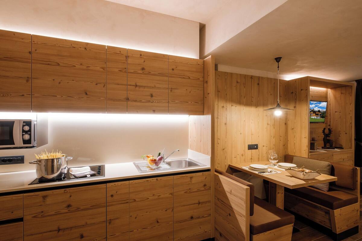 A modern kitchen with wooden cabinetry, a built-in microwave, and a dining area with a wooden table and benches.