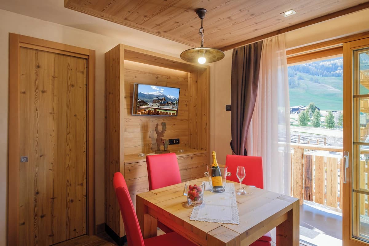 A wooden dining table with red chairs, a bottle of champagne, and a glass on the table.