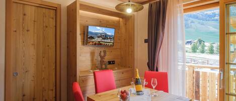 Une table à manger en bois, des chaises rouges, une bouteille de champagne et un verre posés sur la table.