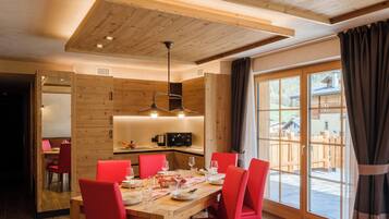Zona pranzo con tavolo in legno e sedie rosse, cucina sullo sfondo e vista su un pontile in legno.