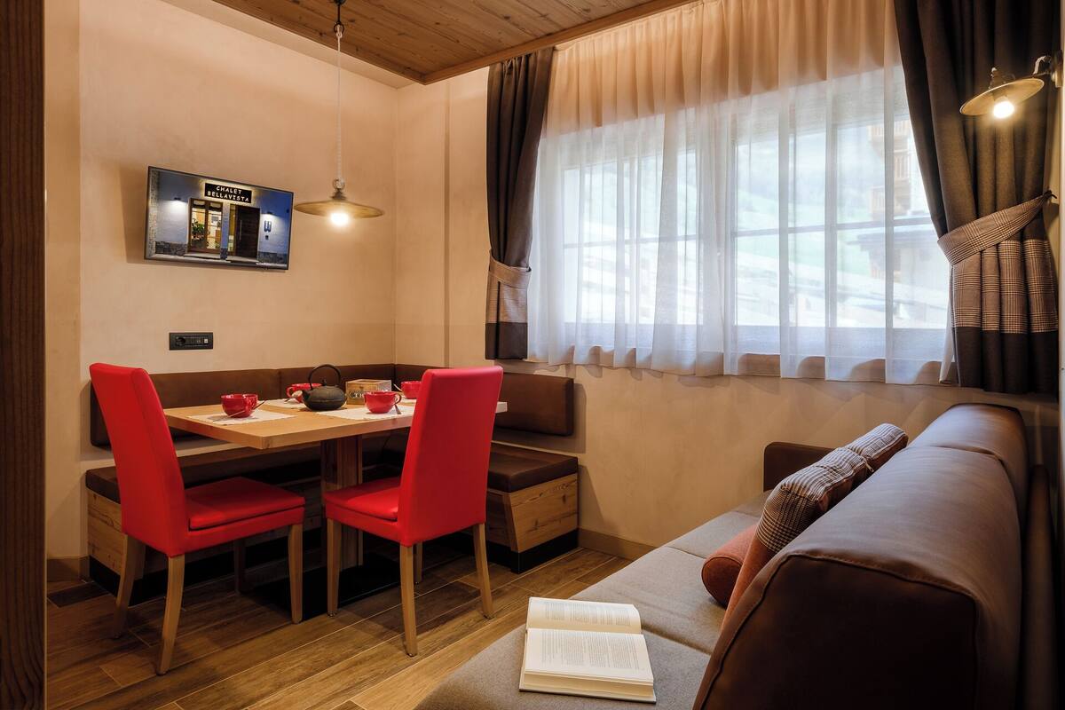 A cozy room with a dining table, red chairs, a sofa, and a window with curtains.