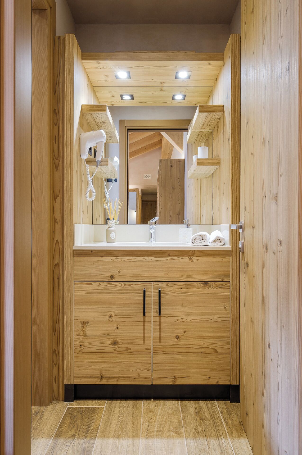 Een houten badkamer met een grote spiegel, een wastafel en een haardroger.